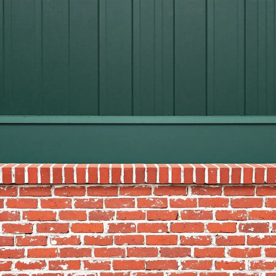 Dark green vertical board and batten siding above a red brick base, with a horizontal band and a brick ledge course where they meet