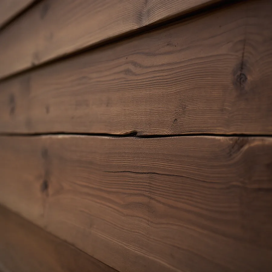 Dark-stained cedar lap siding with one board split lengthwise along the grain
