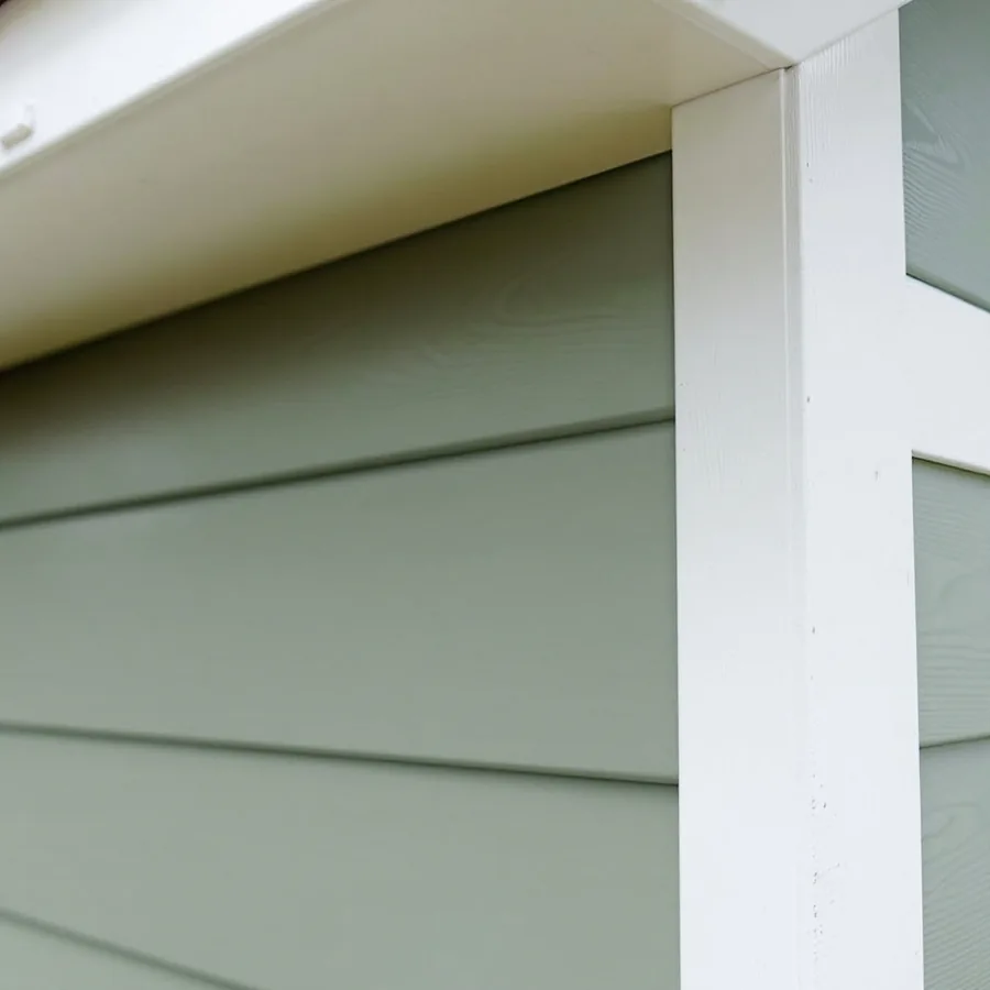 Sage green lap siding planks stopping against a thick white vertical corner board under a white eave
