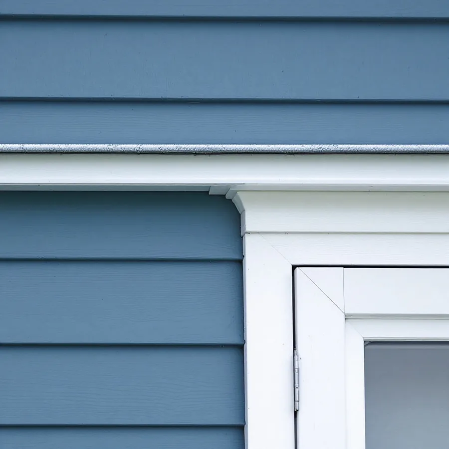 Top corner of a white trimmed window in blue lap siding, with a strip of metal flashing above the head trim