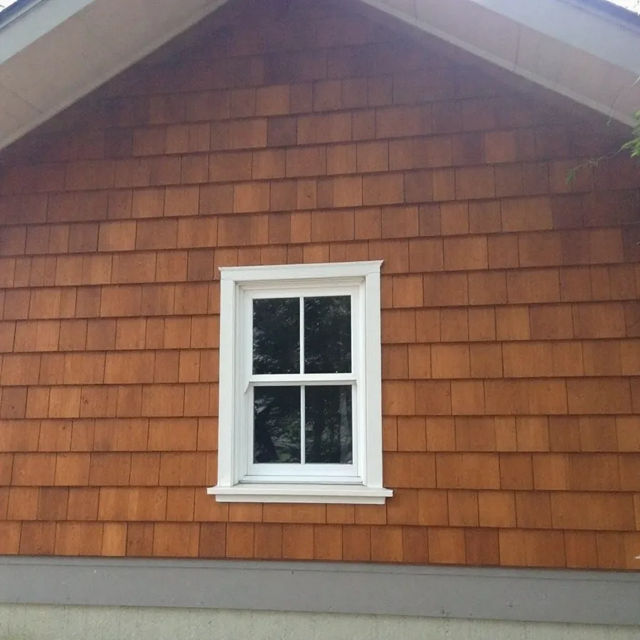 Gable wall covered in honey-brown stained cedar shingles around a small white window
