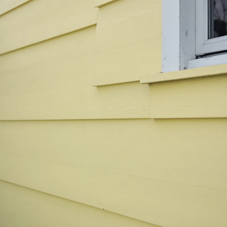 Painted cedar clapboard siding in pale yellow on an older house with a white window casing