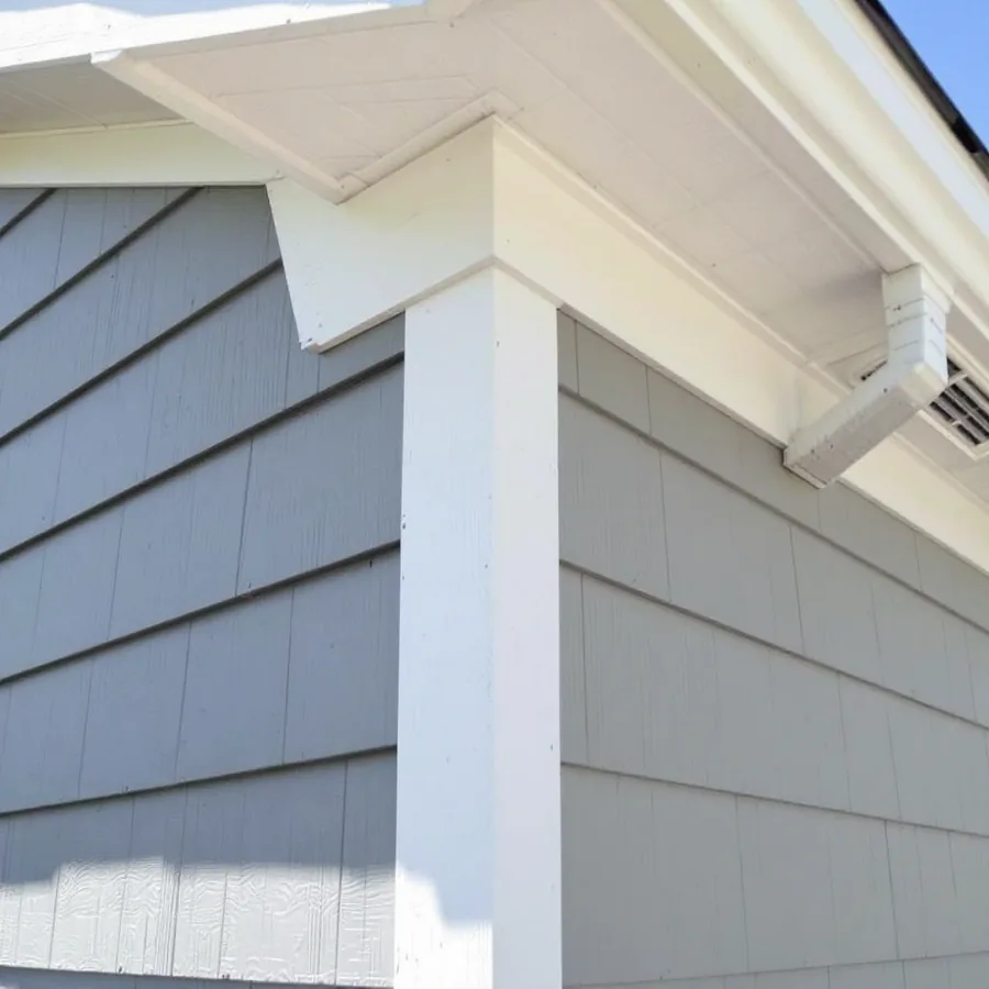 Close view of a house corner where new gray lap siding meets white corner trim boards and a vented soffit above