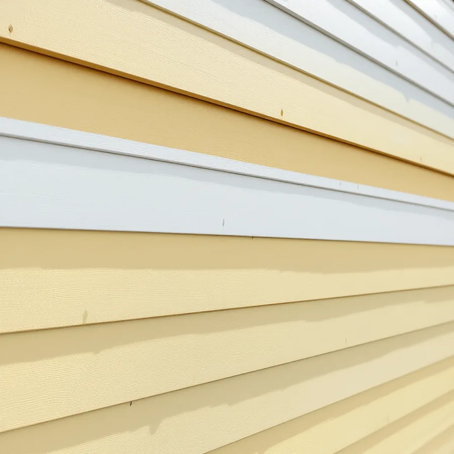 Wall of yellowed cream vinyl siding with one new bright white course among the old courses