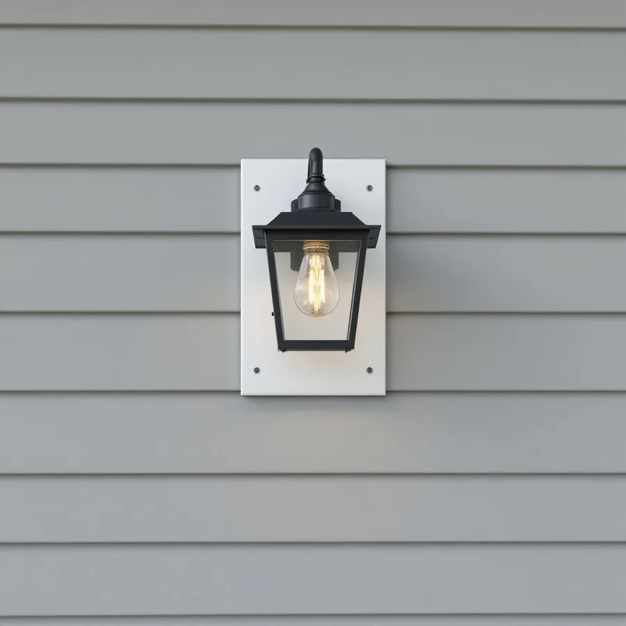 Black wall lantern fastened to a flat white mounting plate on a wall of gray lap siding