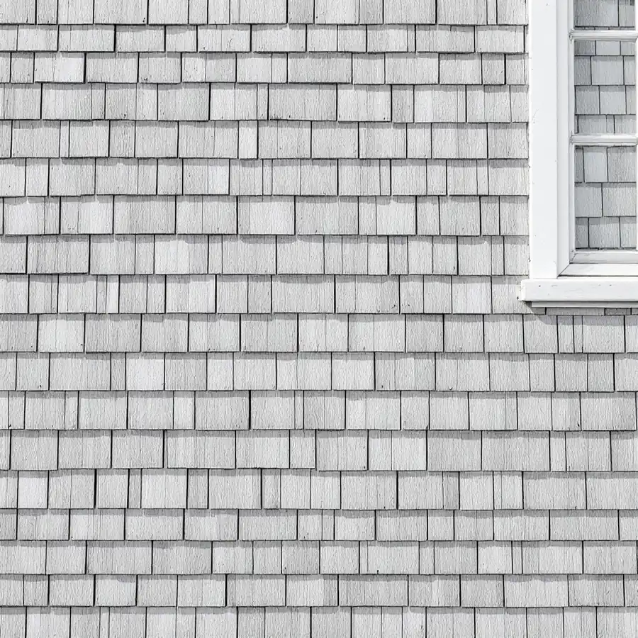 Wall of unfinished wooden shingles weathered to an even silver gray beside a white window frame