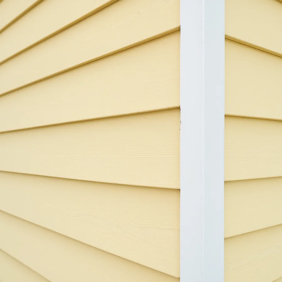 Pale yellow painted wooden lap siding with a crisp white corner board